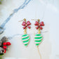 close upof ball stud retro ornament style earrings on a marble background surrounded by foliage.