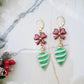 close up of latch back retro ornament style earrings on a marble background surrounded by foliage.