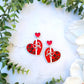 red and white heart earrings on a white marble background surrounded by foliage. 