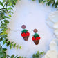 Chocolate covered strawberry earring on white marble background surrounded by foliage. 