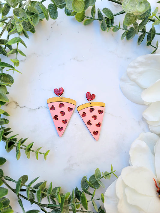 slice of love pizza earrings on a white marble background surrounded by foliage. 
