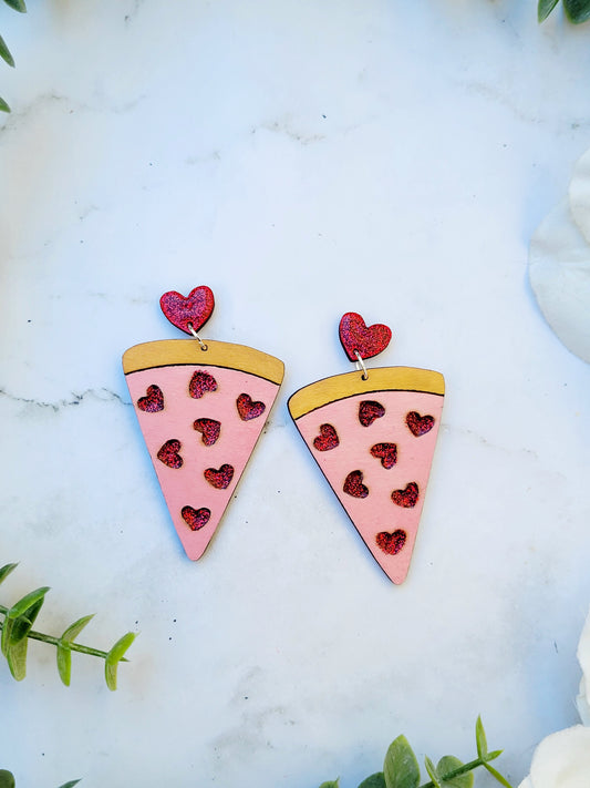 close up of slice of love pizza earrings on a white marble background surrounded by foliage.