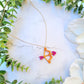 gold and pink cupid's bow necklace on a white marble background surrounded by foliage. 