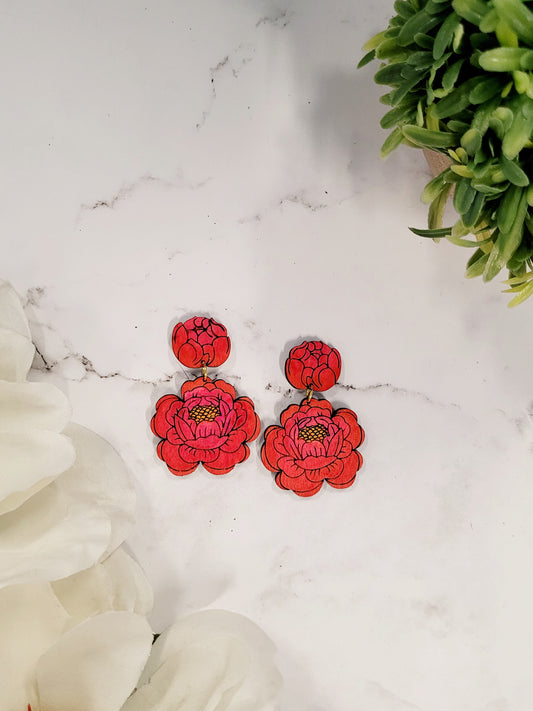 close up of Painted peony earrings on a white marble background surrounded by foliage.