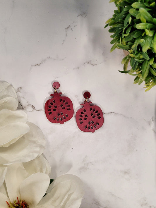 Pomegranate earrings on a white marble background surrounded by foliage