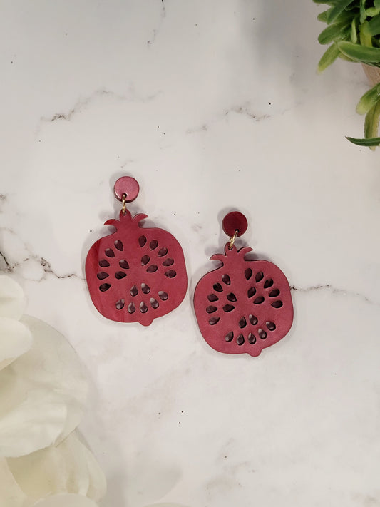 close up of Pomegranate earrings on a white marble background surrounded by foliage
