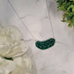 Green pickle necklace on a white marble background surrounded by foliage.