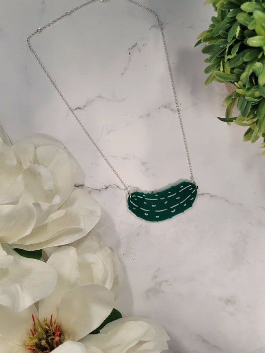 Green pickle necklace on a white marble background surrounded by foliage.