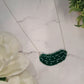 close up of Green pickle necklace on a white marble background surrounded by foliage.