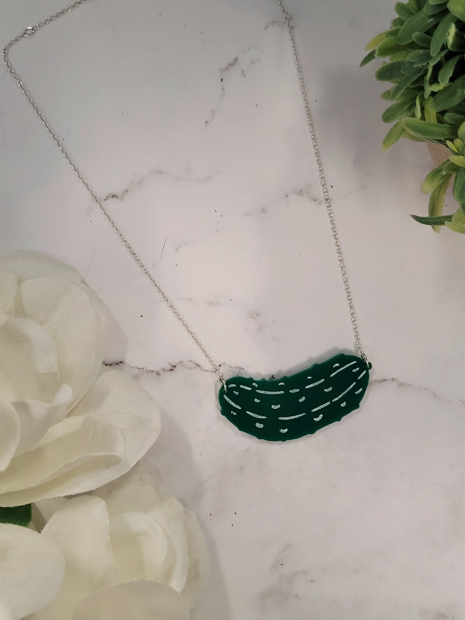 close up of Green pickle necklace on a white marble background surrounded by foliage.