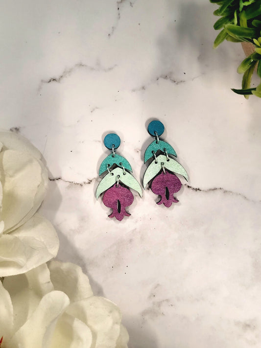 Fuchsia earrings on a marble background surrounded by foliage. 