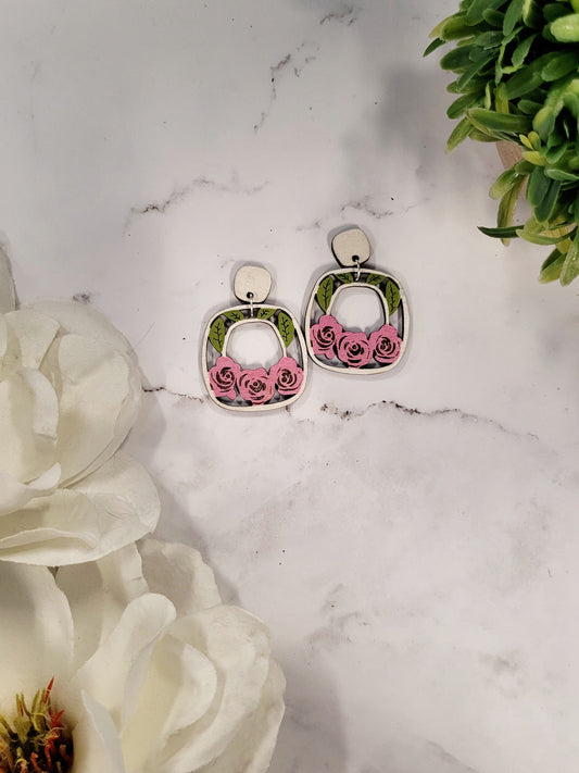 rose garden earrings on a white marble background surrounded by foliage. 
