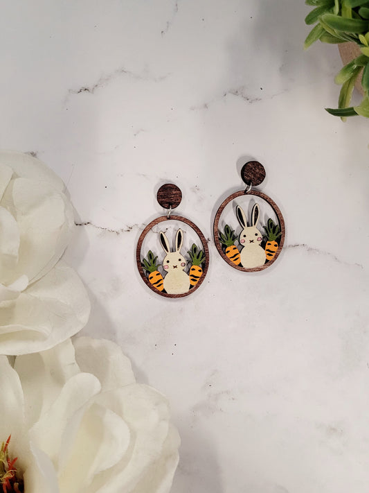 close up of Spring bunny earrings on a white marble background surrounded by foliage.