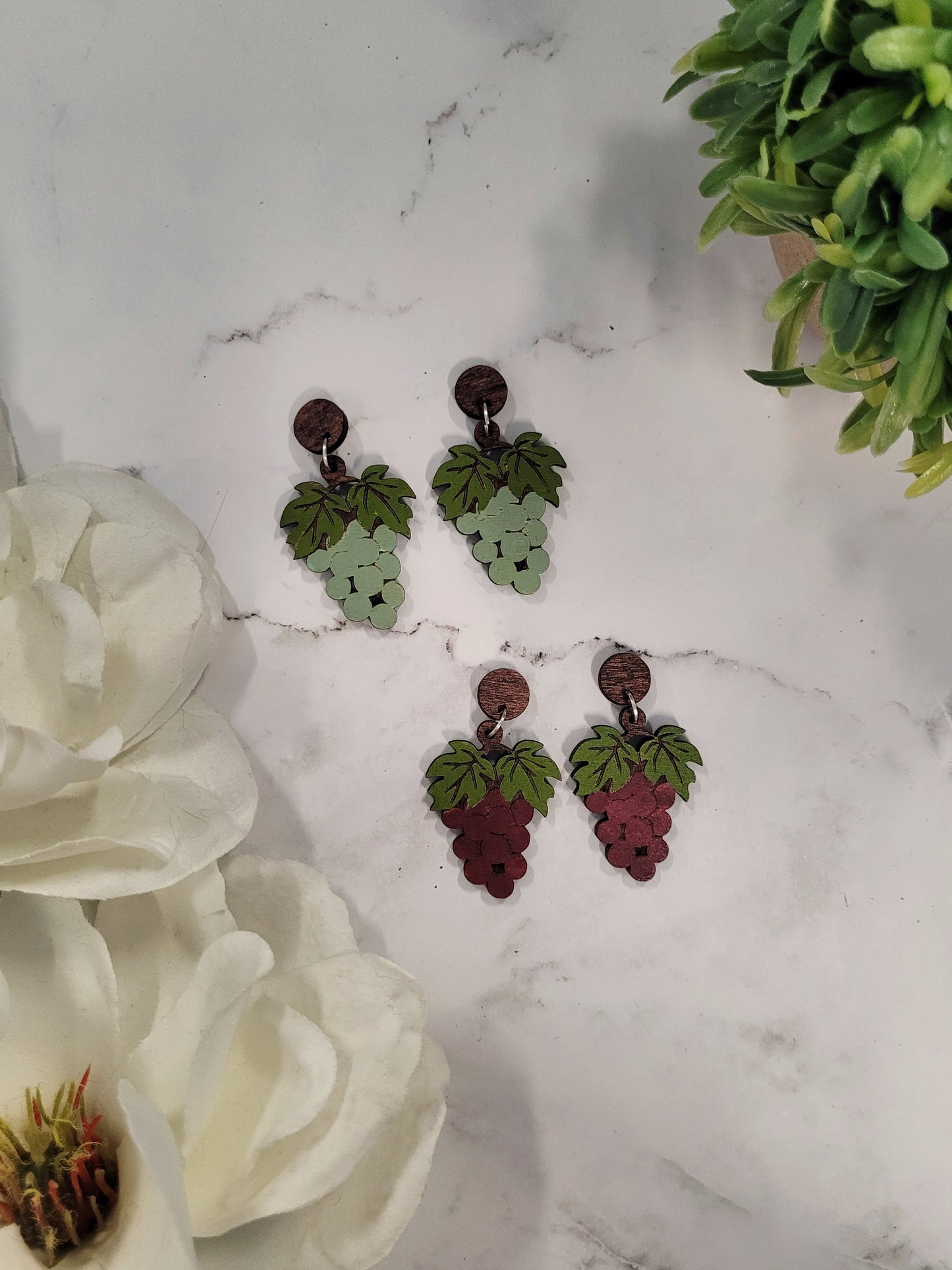 Red and Green grape bunch earrings on a marble background surrounded by foliage 