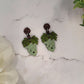 close up of Green grape bunch earrings on a marble background surrounded by foliage