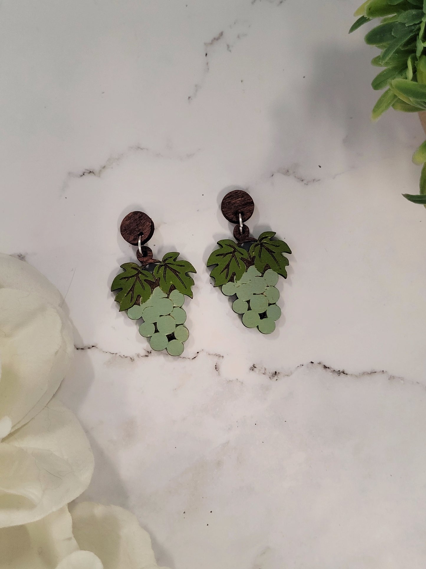 close up of Green grape bunch earrings on a marble background surrounded by foliage