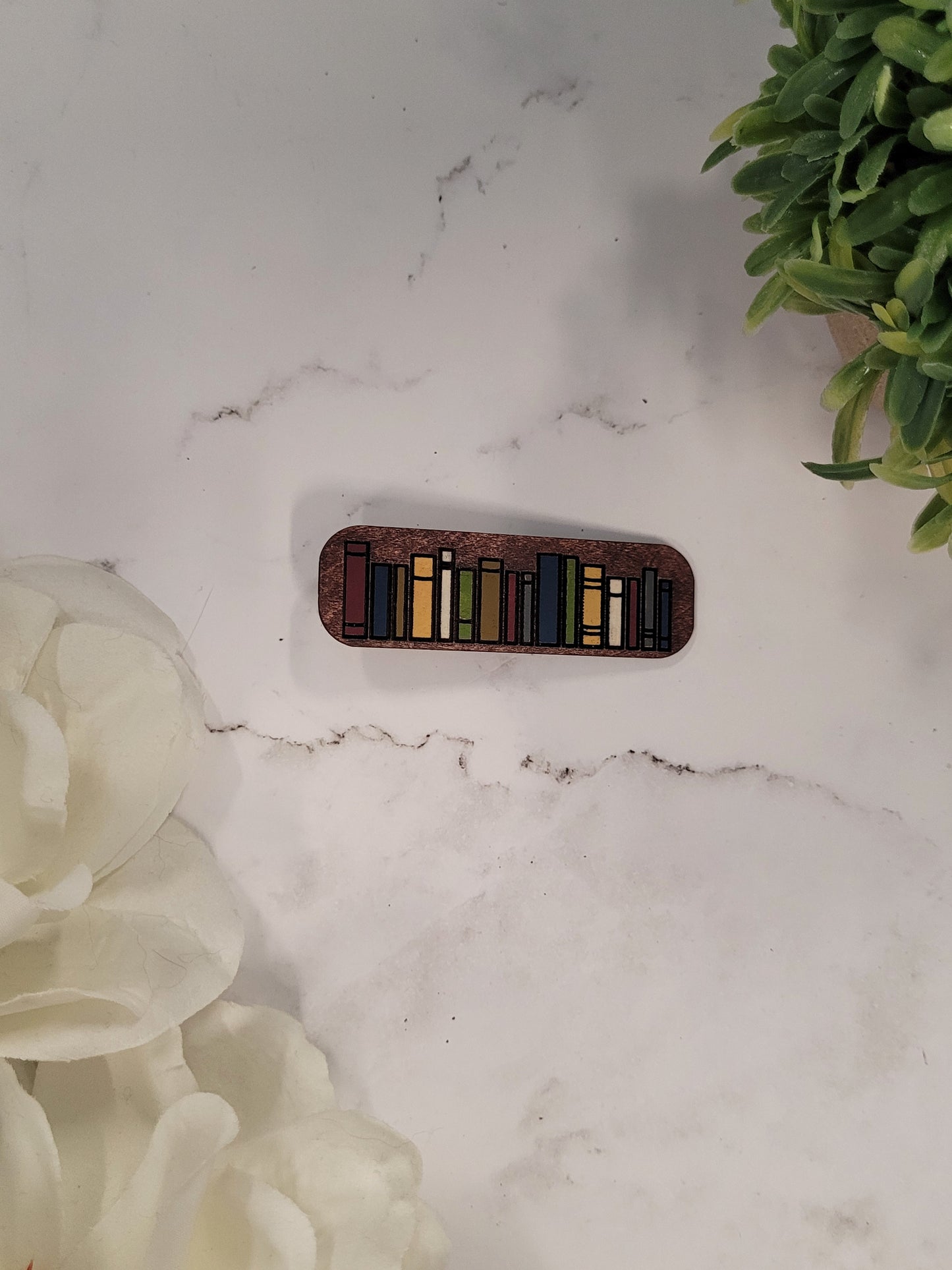 close up of neutral book hair clips on a white marble background surrounded by foliage.