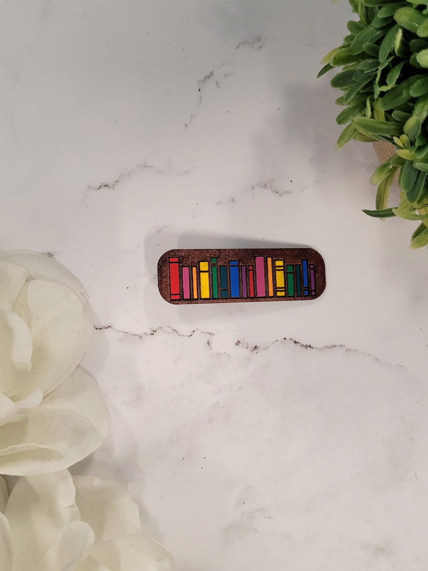 close up of rainbow book hair clips on a white marble background surrounded by foliage.