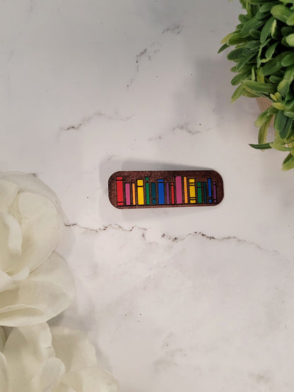 close up of rainbow book hair clips on a white marble background surrounded by foliage.