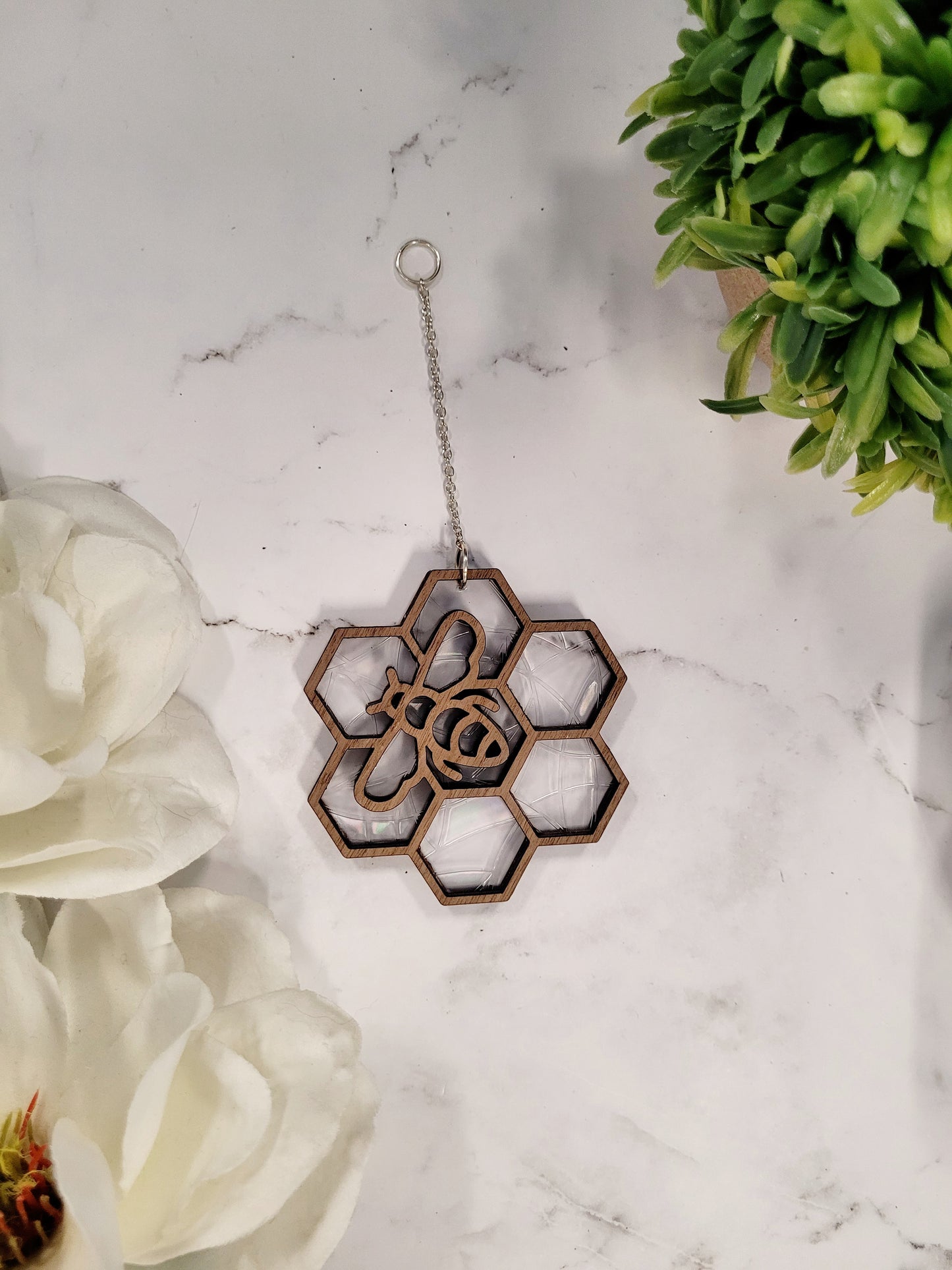 Bee suncatcher on marble background surrounded by foliage. 