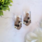 wooden beehive shaped earrings with bee charms on a marble background surrounded by foliage. 