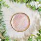 faux mother of pearl trinket dish with gold detailing on a marble background surrounded by foliage.