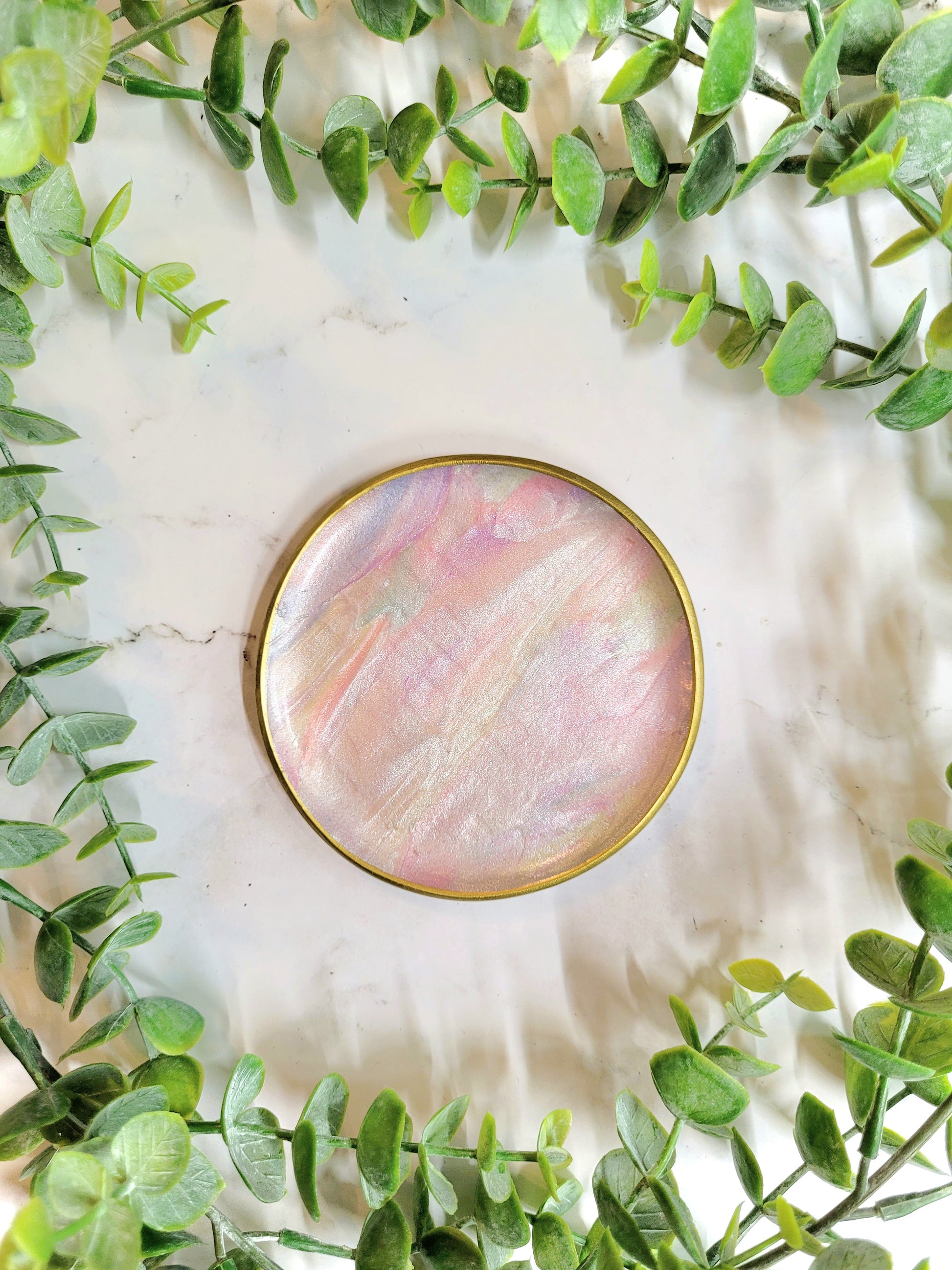 faux mother of pearl trinket dish with gold detailing on a marble background surrounded by foliage.