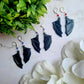Three bat boy earrings on a marble background surrounded by foliage.