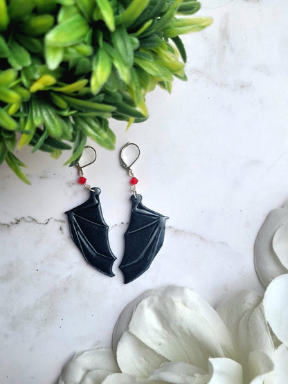 close up of red bat boy earrings on a marble background surrounded by foliage.