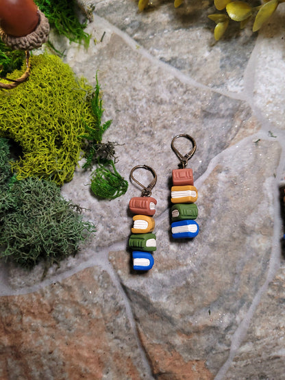 Mini sized Cottagecore bookstack earrings on a stone background surrounded by moss and foliage. 
