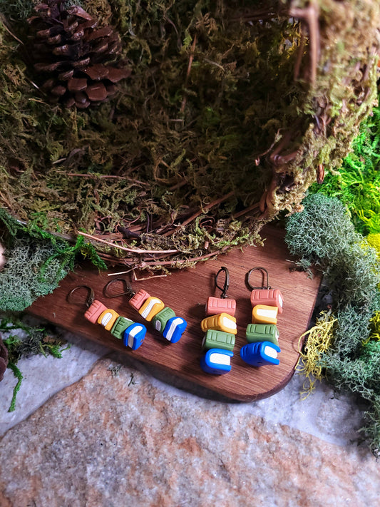 Cottagecore bookstack earrings on a wood and stone background surrounded by moss. 