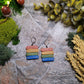 Gilded bookstack earrings on a stone background surrounded by moss and foliage. 