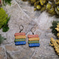 close up of Gilded bookstack earrings on a stone background surrounded by moss and foliage. 