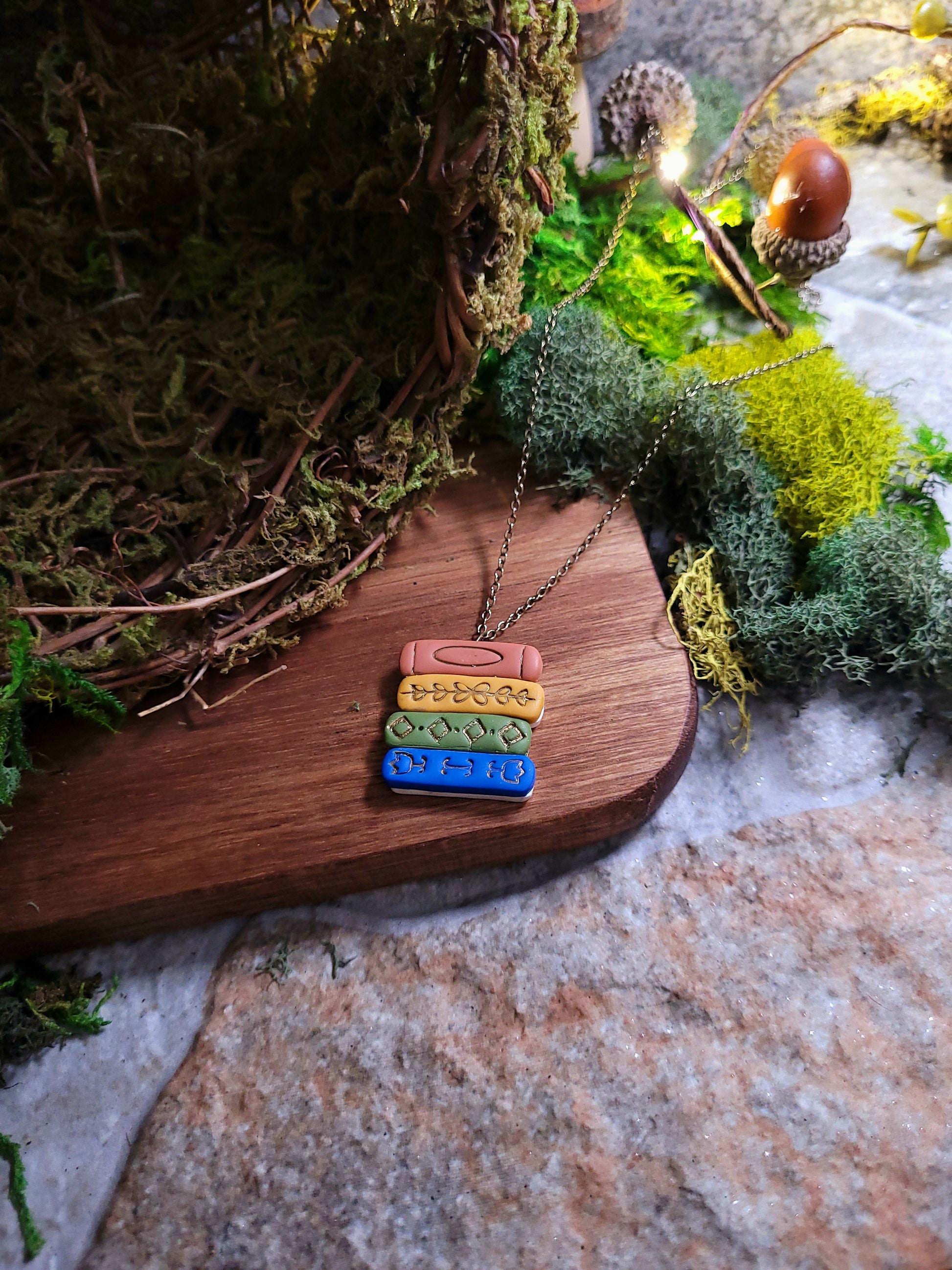 Gilded bookstack necklace on wood and stone background surrounded by moss