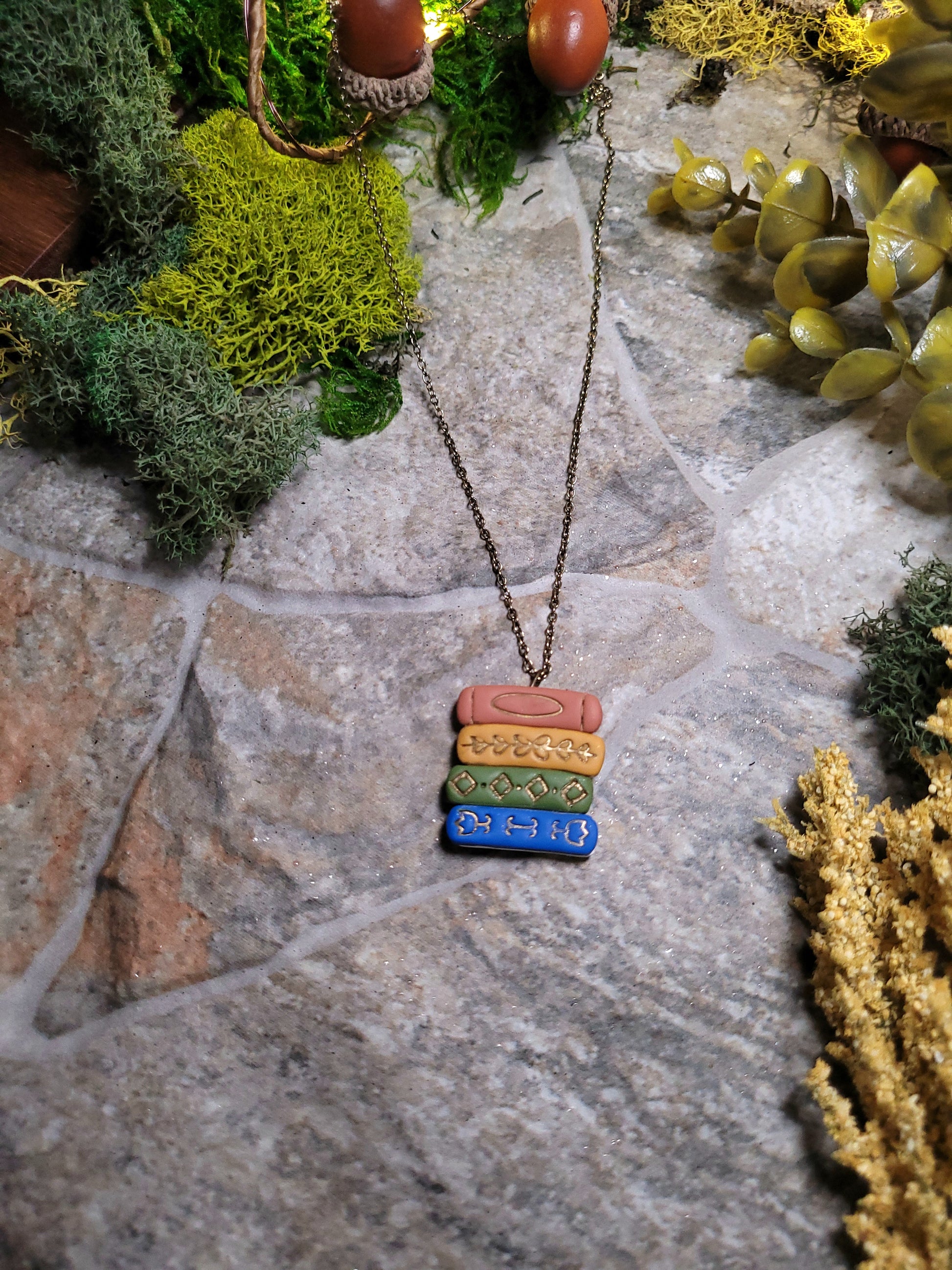 Gilded bookstack necklace on stone background surrounded by moss and foliage