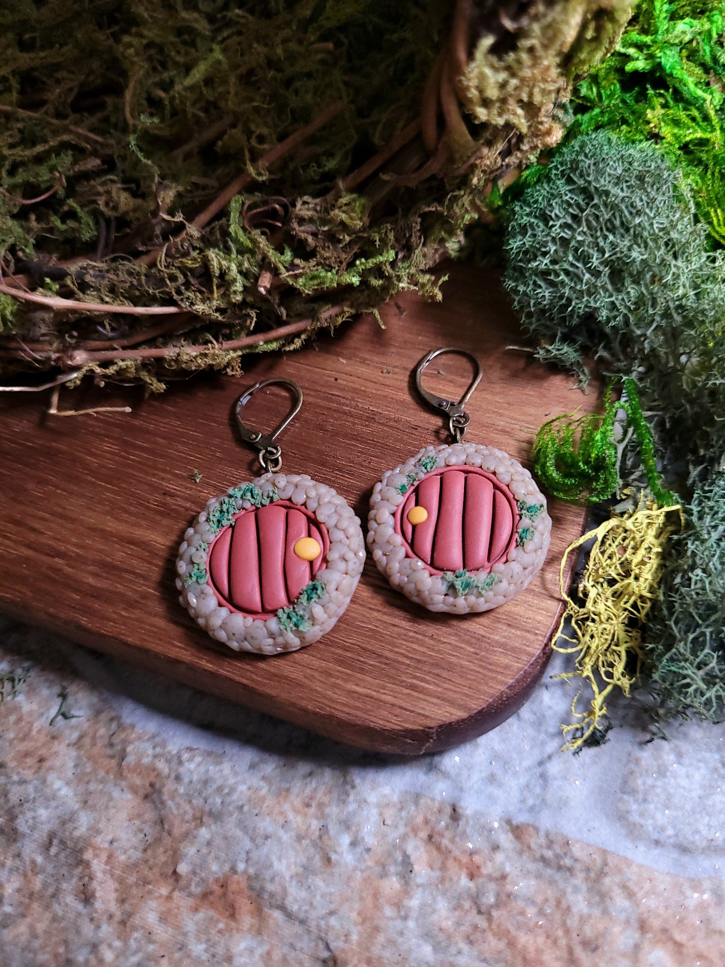 close up of fairy door earrings on wood and stone background surrounded by moss