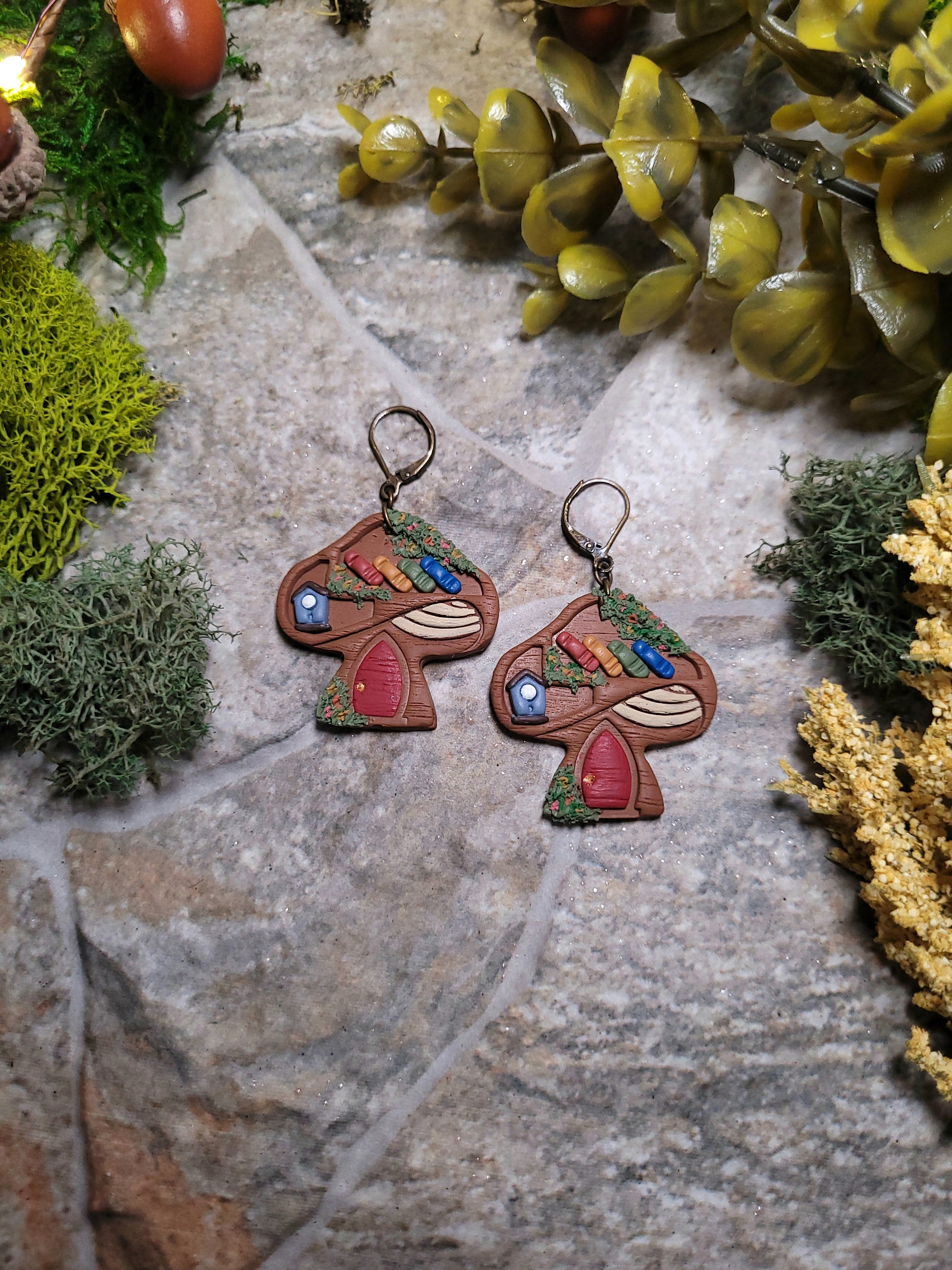 Mushroom Shelf Earring on a stone background surrounded by foliage. 