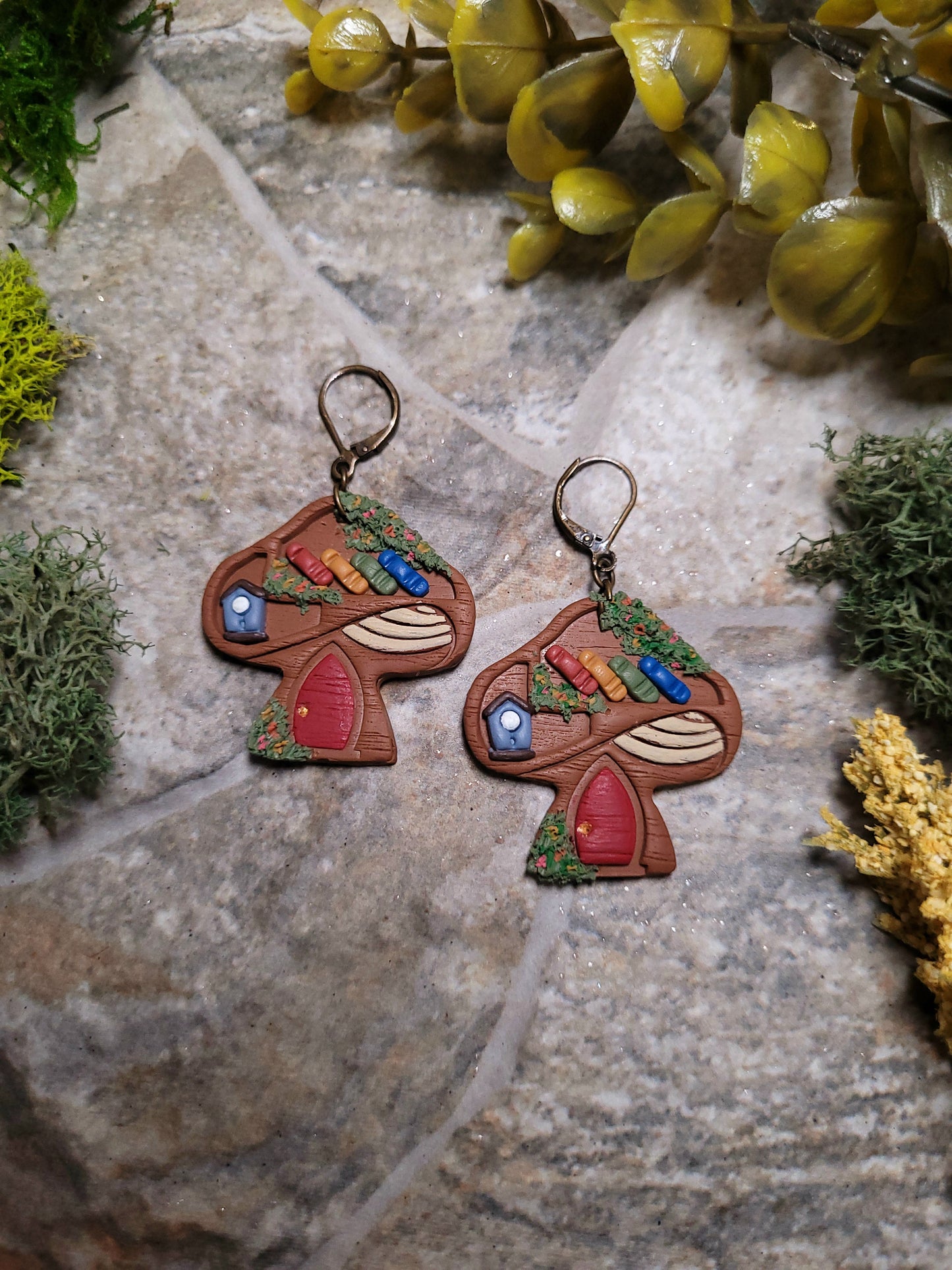 close up of Mushroom Shelf Earring on a stone background surrounded by foliage. 