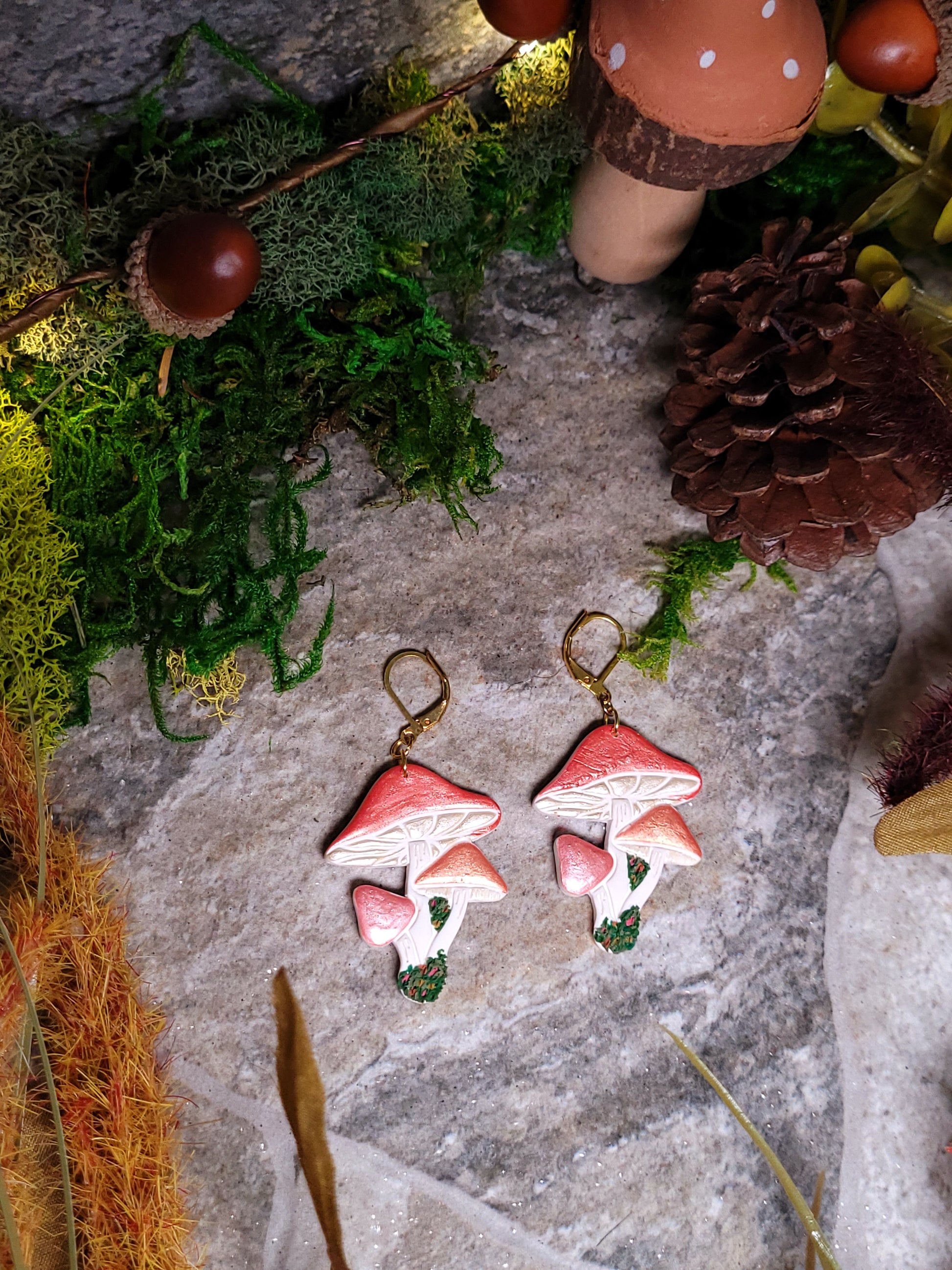 Shroom earrings on a stone background surrounded by foliage. 