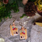 charcuterie board earrings on a stone background surrounded by foliage. 