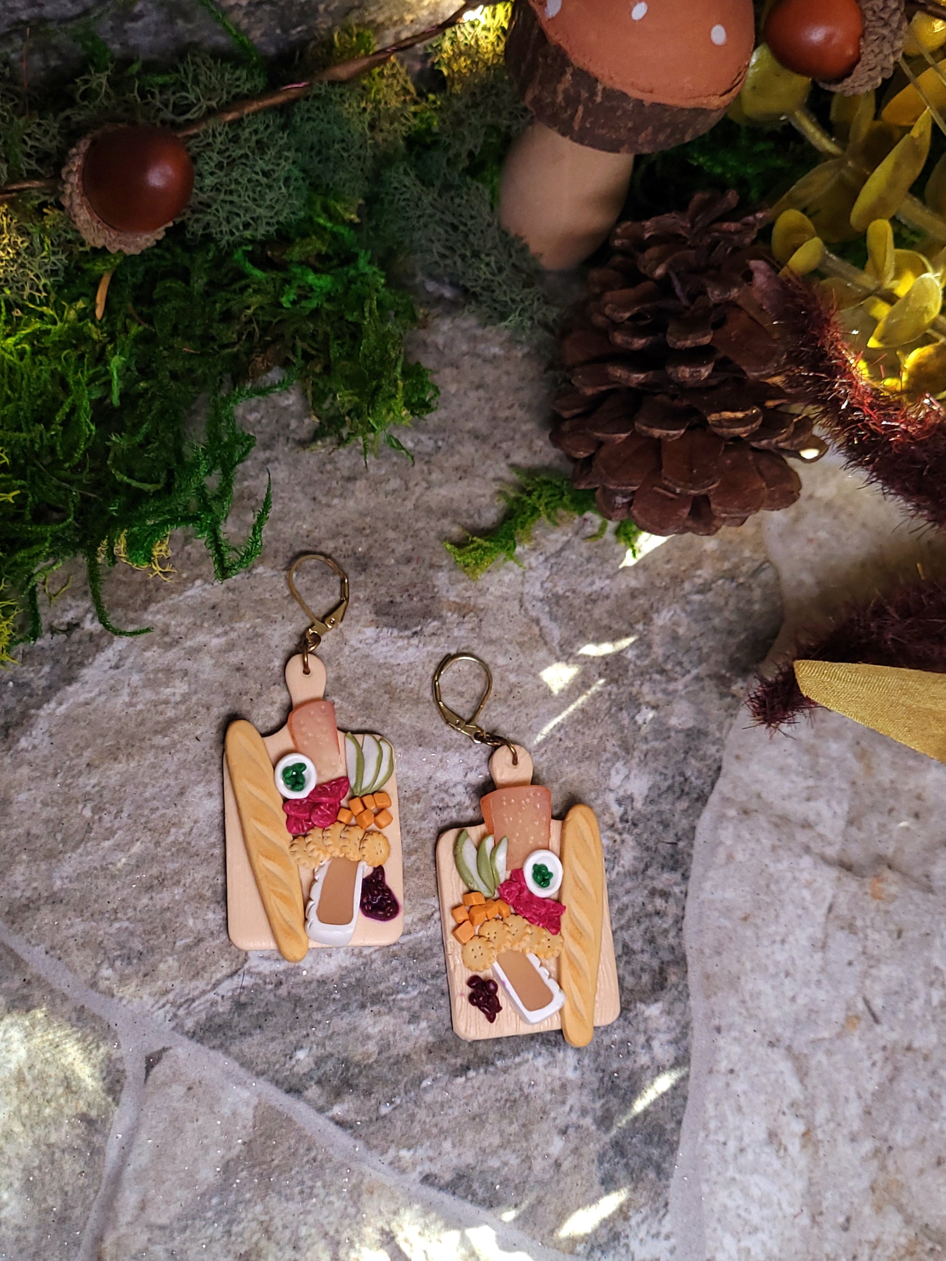 charcuterie board earrings on a stone background surrounded by foliage. 