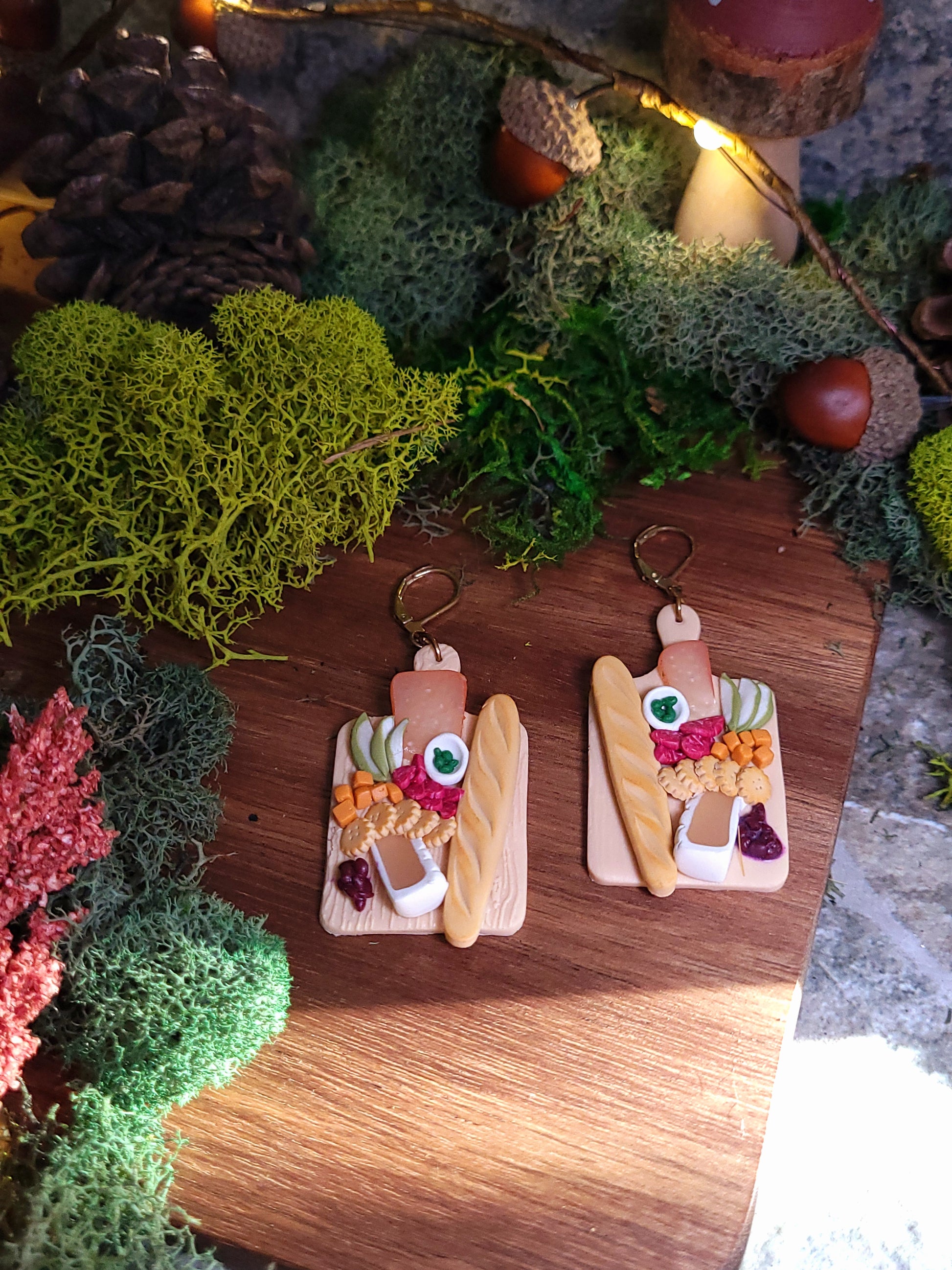 charcuterie board earrings on a wood and stone background surrounded by foliage. 