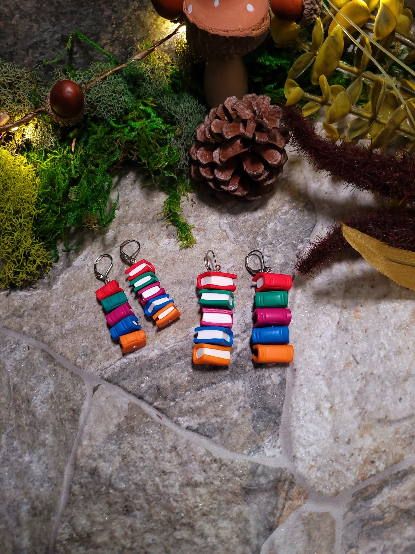 Back and side view of Bookstack earrings made of polymer clay in two sizes sits on a stone background surrounded by foliage.