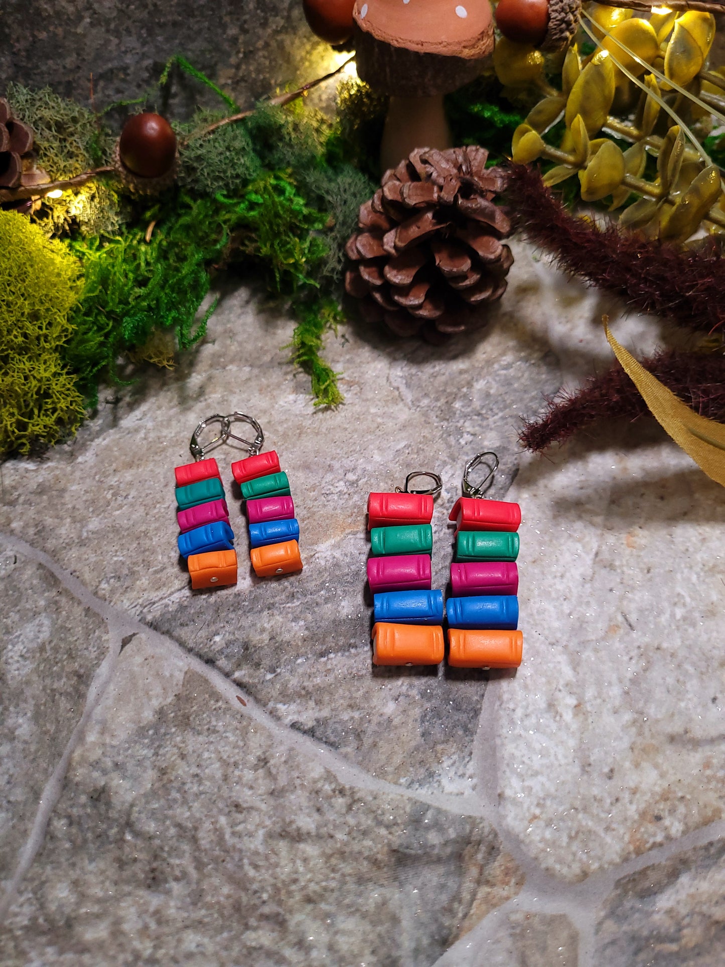 back view of Bookstack earrings made of polymer clay in two sizes sits on a stone background surrounded by foliage.