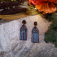 Cathedral window earrings on a stone background surrounded by foliage.