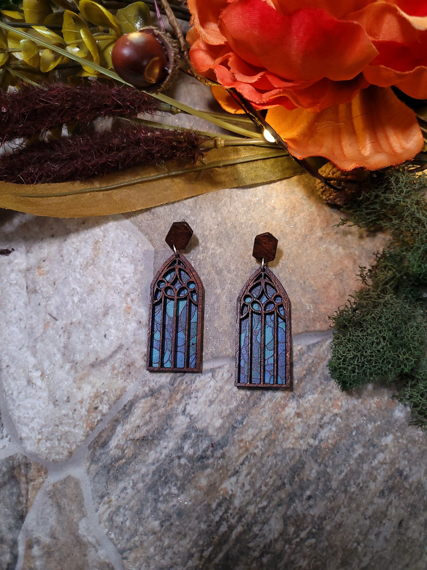 Cathedral window earrings on a stone background surrounded by foliage.