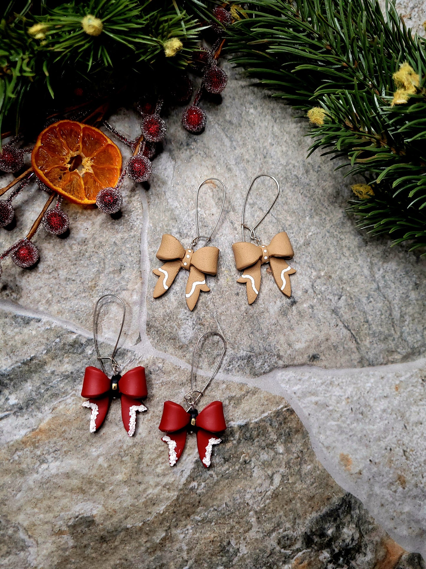 Christmas Bow Earrings on a  stone background surrounded by foliage