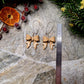 Gingerbread Bow earrings on a  stone background surrounded by foliage