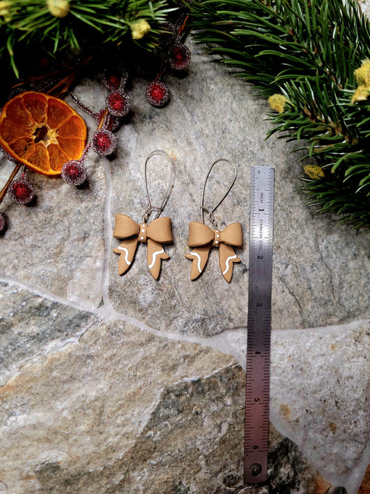 Gingerbread Bow earrings on a  stone background surrounded by foliage