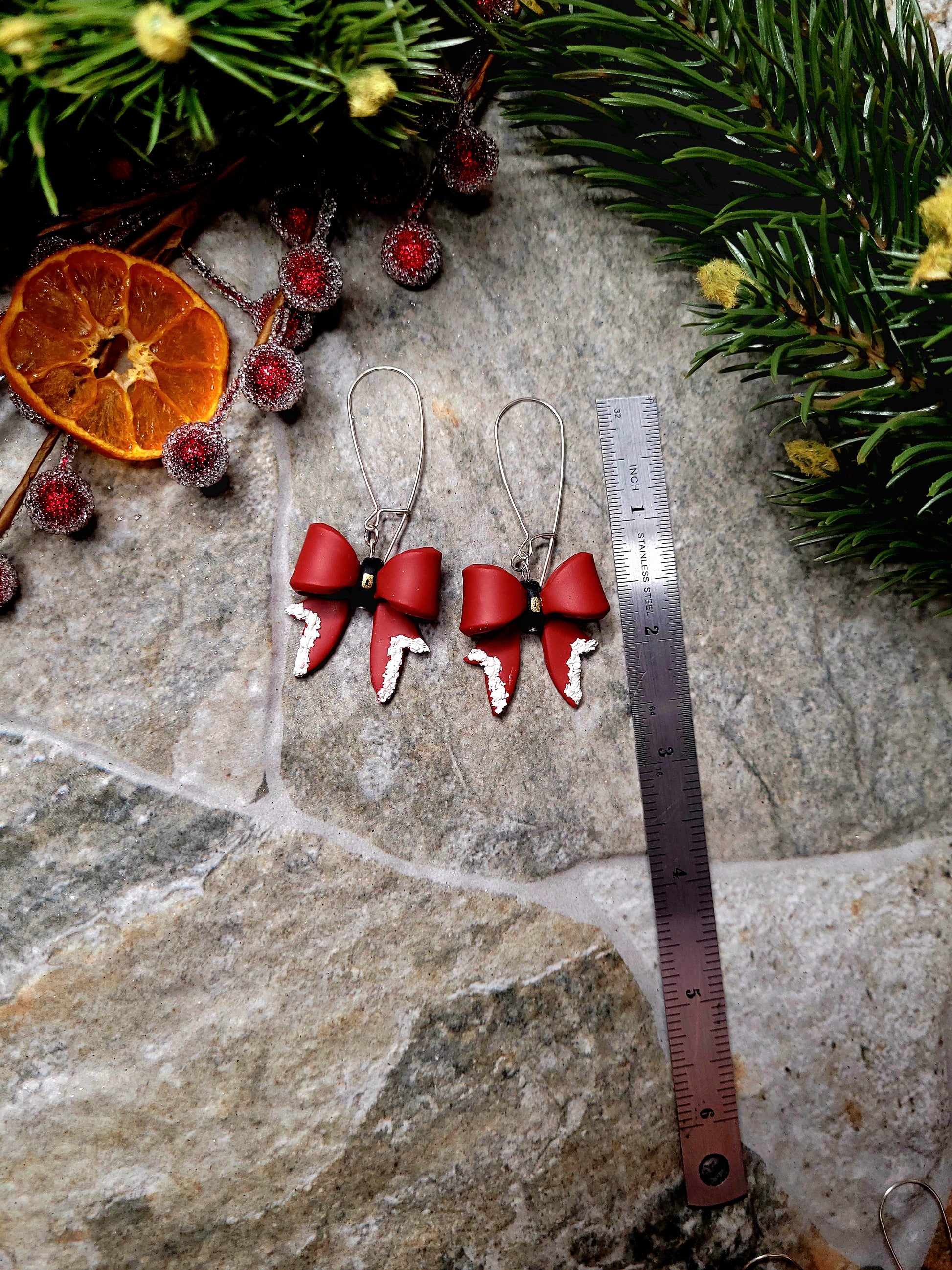 Santa Bow earrings on a  stone background surrounded by foliage